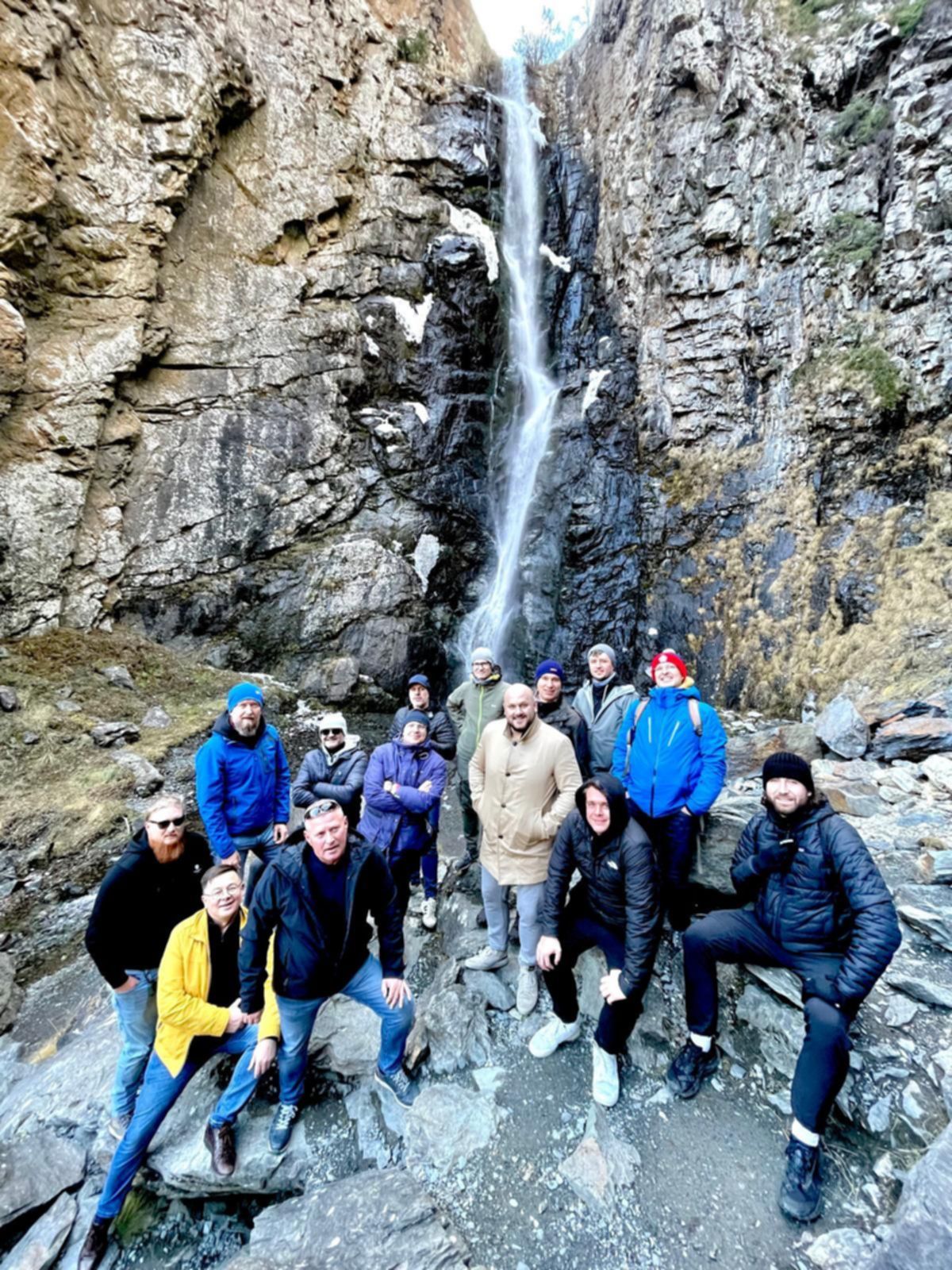 Grupa turystów przy wodospadzie Gveleti w Kazbegi, skalna ściana i spływająca kaskada w tle