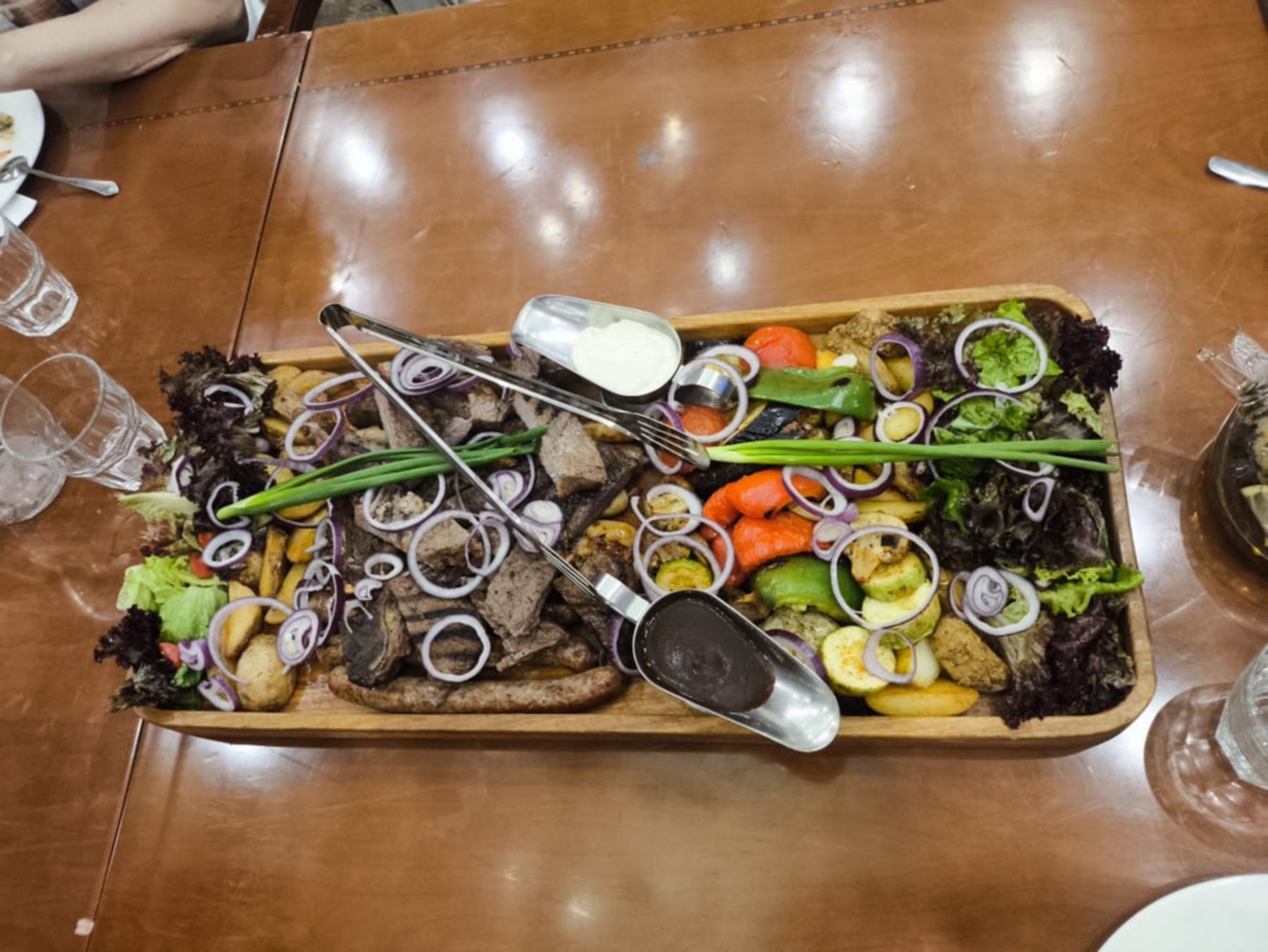 Tradycyjne danie kuchni kazachskiej serwowane na dużej drewnianej tacy – grillowane warzywa, mięsa, ziemniaki, świeże zioła oraz sosy, podane podczas wspólnej kolacji.