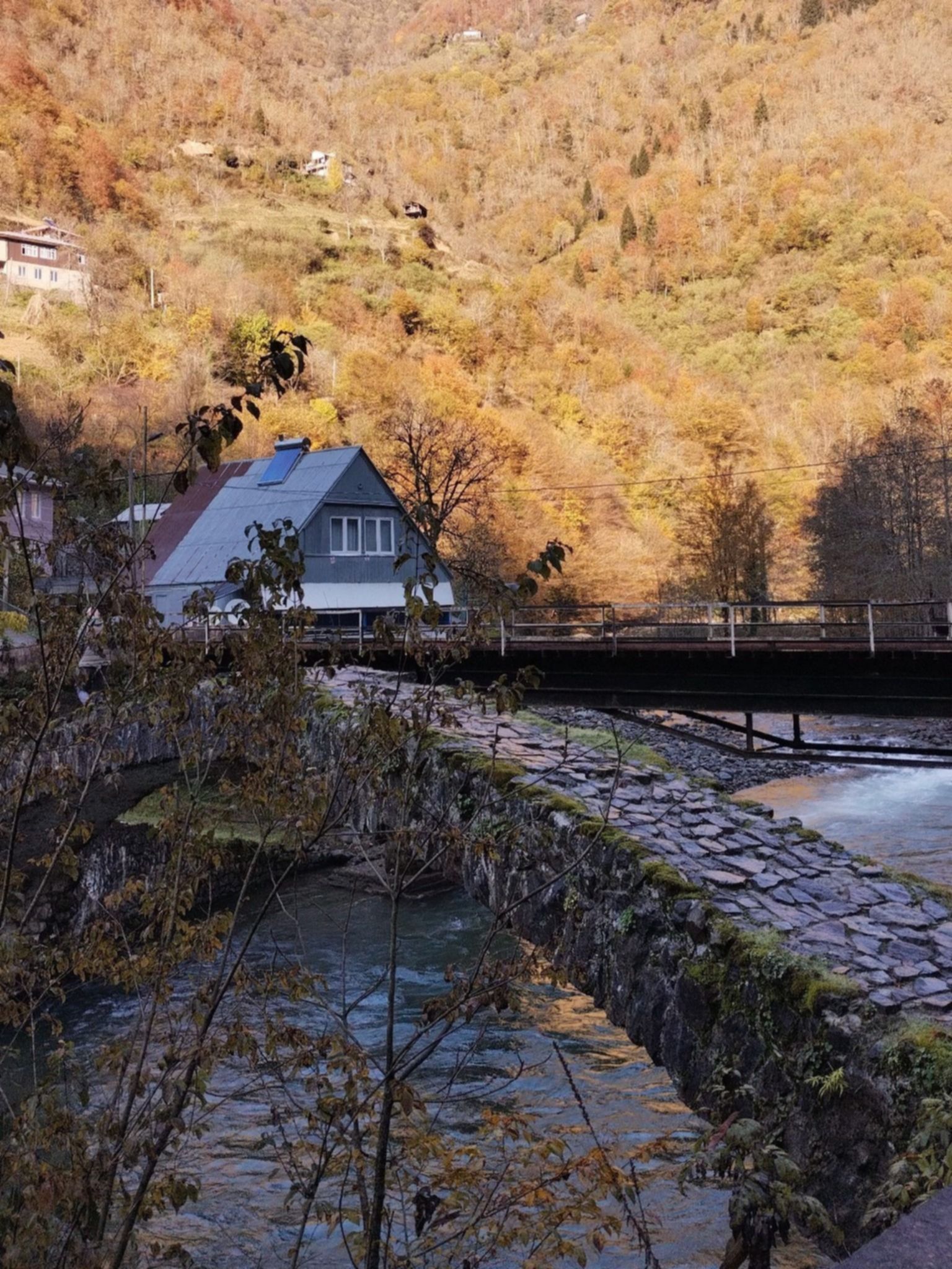 Kamienny most Cchemlara w górskiej wsi w Adżarii, Gruzji – jesienny krajobraz, rzeka i lokalna zabudowa